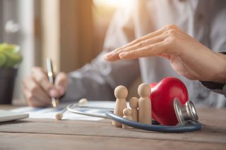 Foto: Eine Hand schützt eine hölzerne Familienfigur